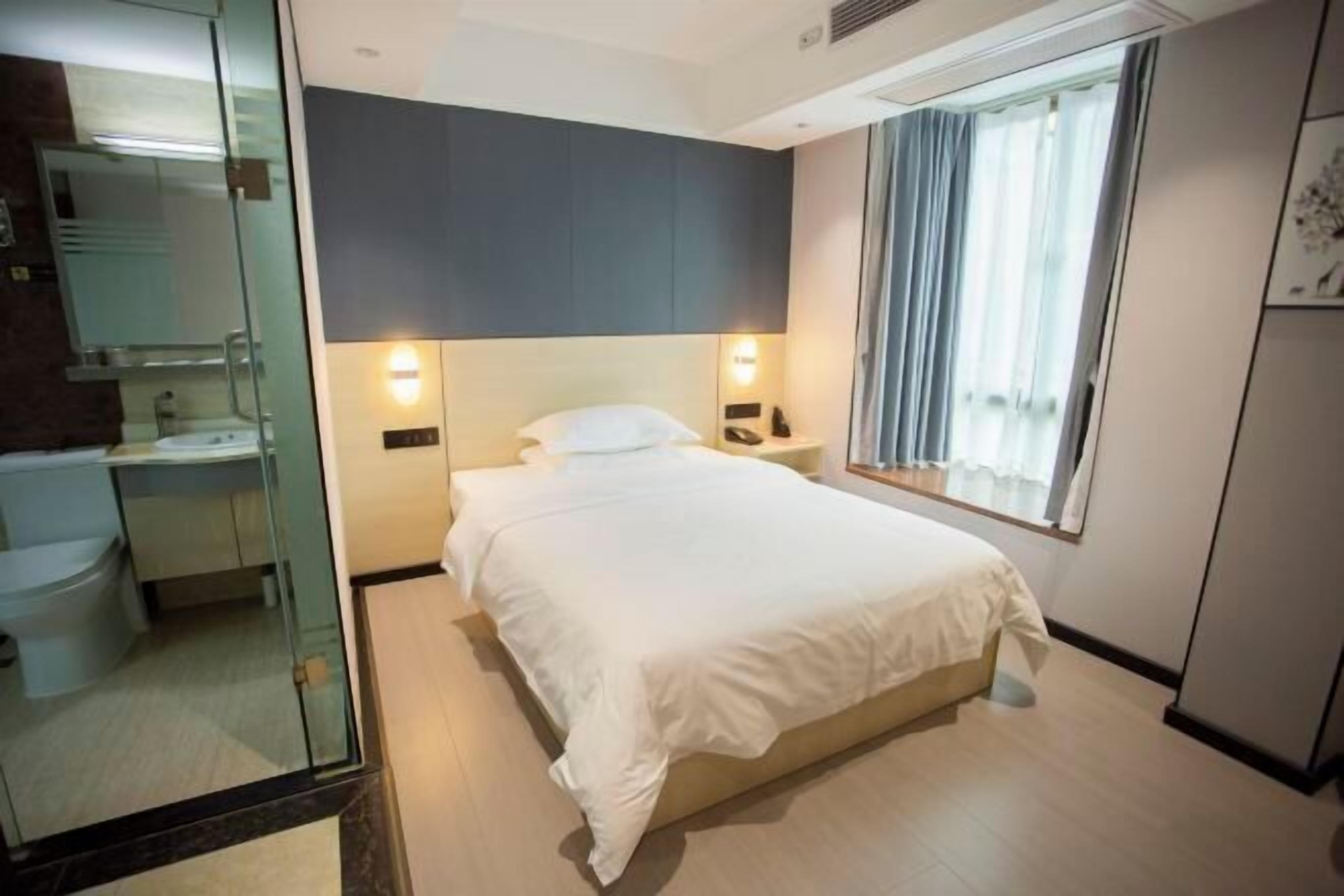 Ein Hotelzimmer mit Bett, Nachttisch, Lampe und einem Fenster mit Vorhängen.