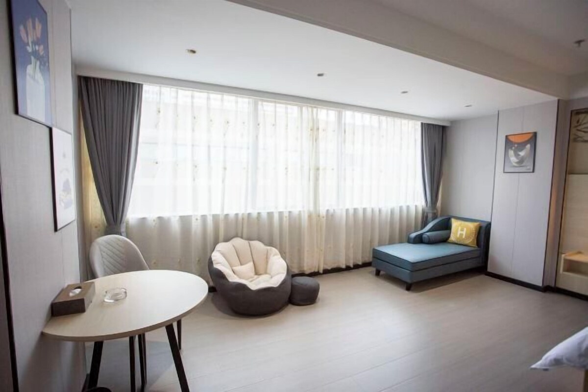 A modern room with a round table, a bean bag chair, a sofa, and a large window with curtains.