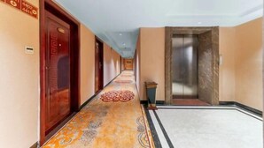 A hotel corridor with a patterned carpet, wooden doors, and an elevator. - Xiangju Business Hotel (Qingyuan Gulongxia Meilin Plaza) (Qingyuan)