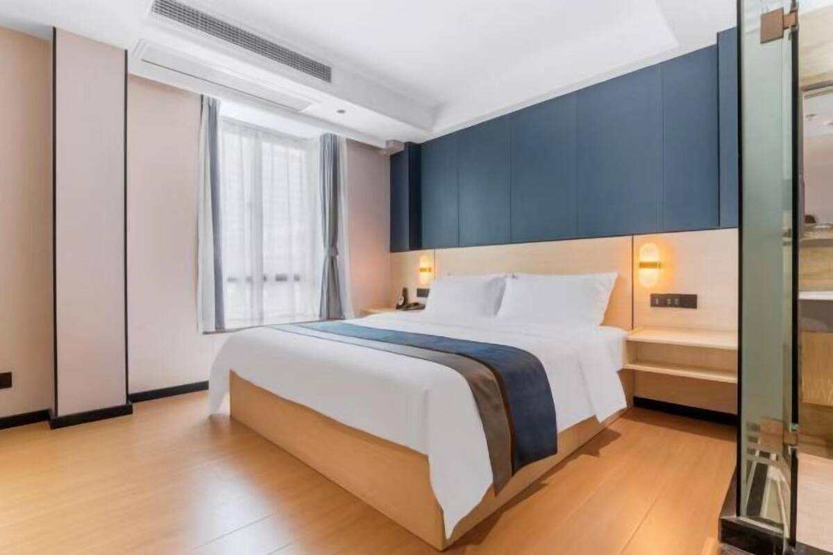 Ein modernes Hotelzimmer mit einem großen Bett, einem Nachttisch, Vorhängen und einem Fenster.