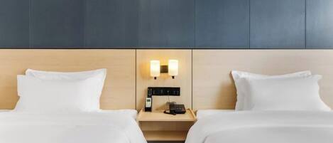 A hotel room with two beds, a nightstand with a phone and lamp, and a wall-mounted light fixture.