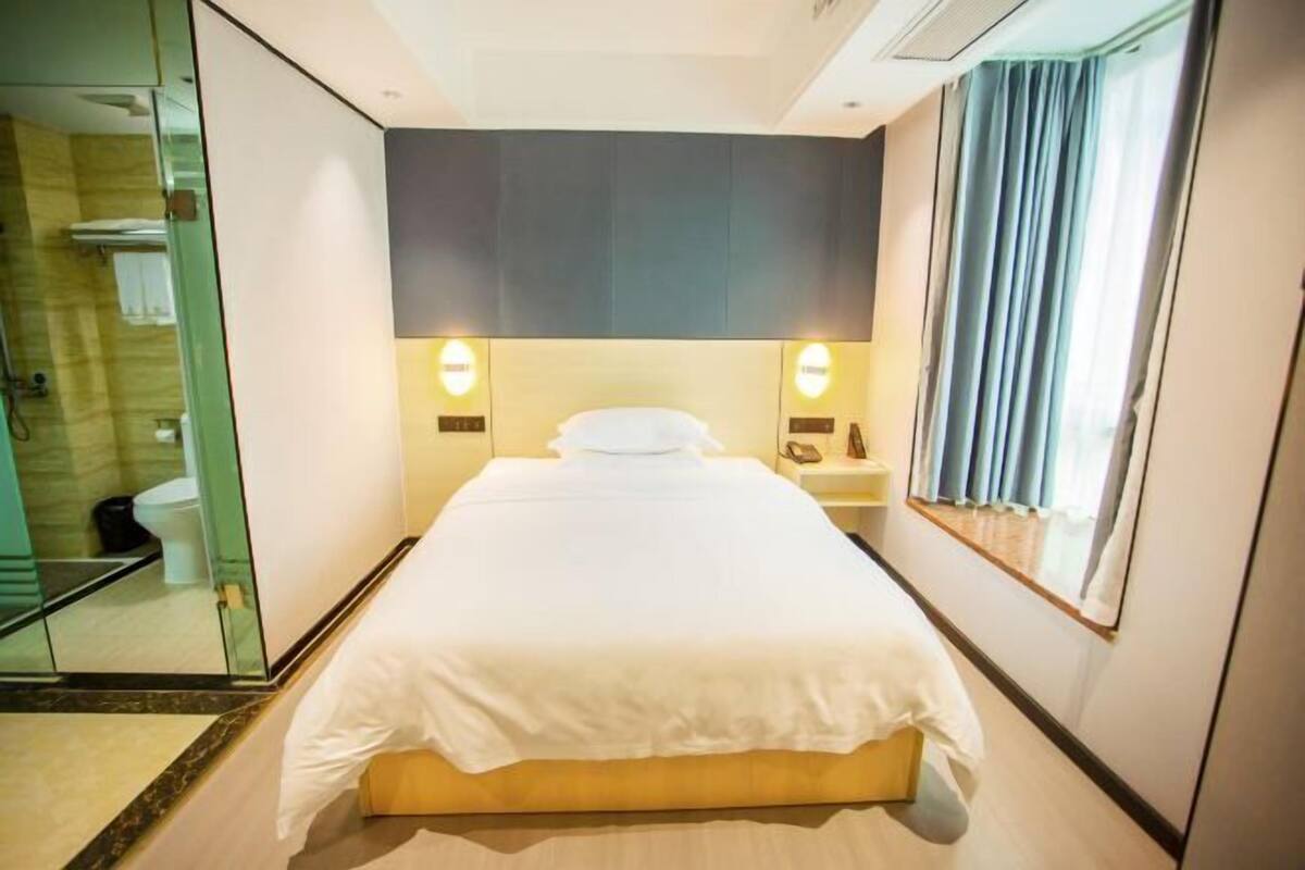 Ein Hotelzimmer mit einem großen Bett, Nachttischlampen, einem Fenster mit Vorhängen und einem Spiegel an der Wand.
