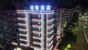 A multi-story hotel with illuminated signage, a modern architectural design, and a visible ground floor with shops. - Xiangju Business Hotel (Qingyuan Gulongxia Meilin Plaza) (Qingyuan)