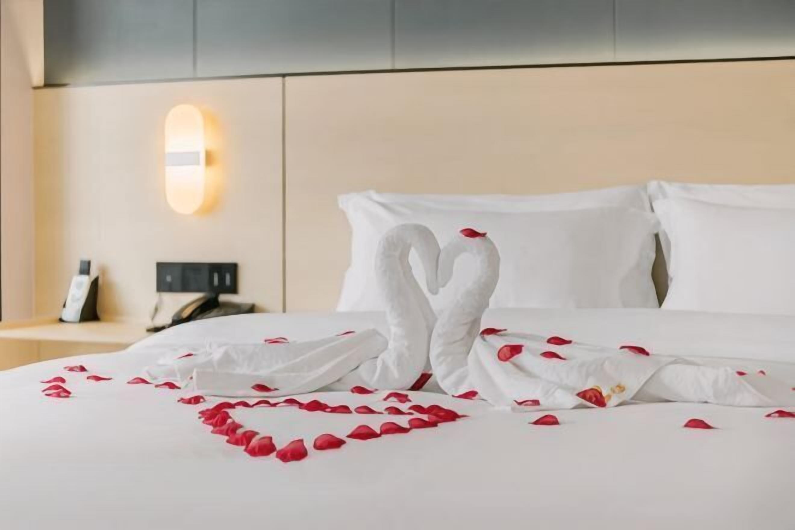 A hotel room with a bed, a nightstand, and a wall-mounted light fixture.