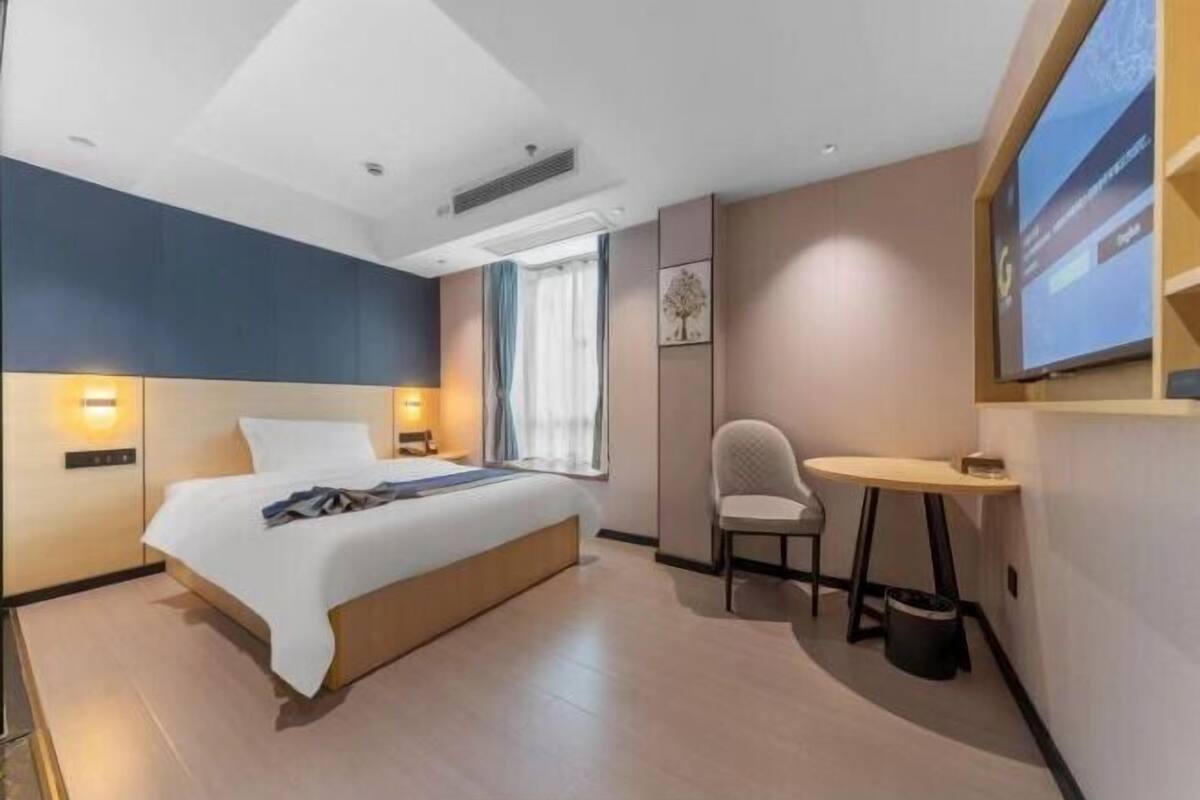 Ein modernes Hotelzimmer mit Bett, Nachttischlampen, einem kleinen Tisch, einem Sessel und einem an der Wand montierten Fernseher.