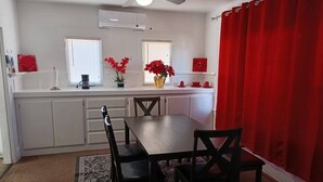 A compact kitchen with white cabinets, a dining table with four chairs, and a red curtain.