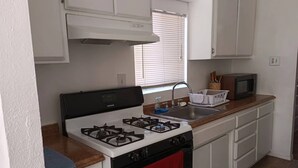 A compact kitchen with white cabinets, a gas stove, a microwave, and a sink.