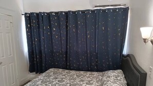 A bedroom with a bed, a dark curtain with a pattern, a wall-mounted light, and a door.