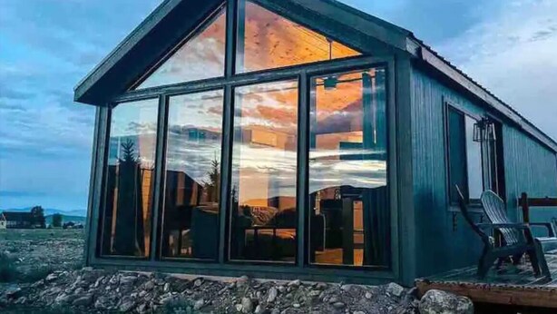 Un bâtiment moderne, de plain-pied, doté de grandes fenêtres en verre qui reflètent les couleurs d’un coucher de soleil.