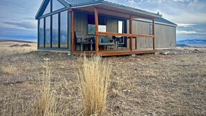 Une cabane moderne dotée de grandes fenêtres, d’une terrasse en bois et offrant une vue sur le paysage environnant.