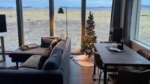 Un salon moderne avec une grande fenêtre, un canapé confortable, un petit sapin de Noël et un coin repas.