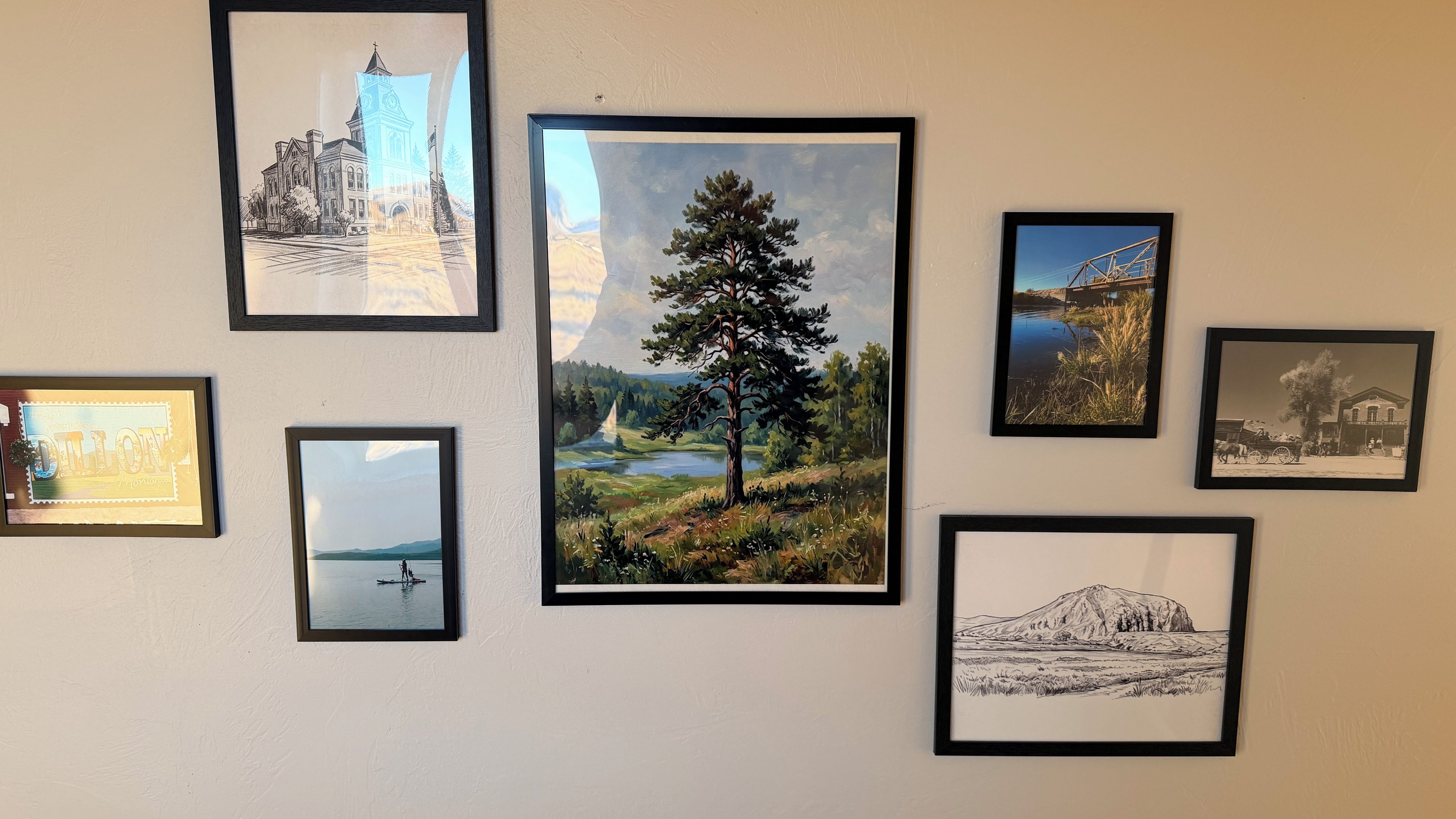 A wall with various framed artworks including landscapes, a building, and a mountain scene.