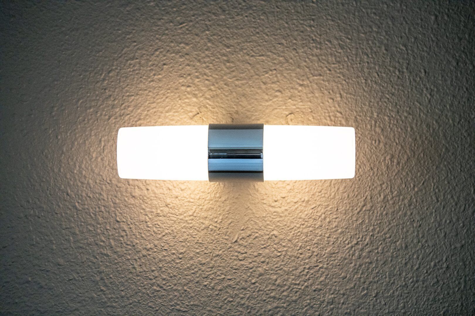 A wall-mounted light fixture with a rectangular shape and a metallic finish.