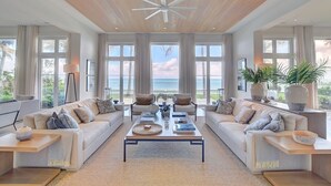 A spacious living room with a large wooden ceiling, two sofas facing a large window overlooking the ocean, and a central coffee table with books and decorative items. - Paradise Beach Villa, OCEANFRONT~Paradise Island~ (Paradise Island)