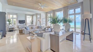 A spacious living room with a large sofa set, a coffee table, and a TV. There is a large window with a view of the ocean. - Paradise Beach Villa, OCEANFRONT~Paradise Island~ (Paradise Island)