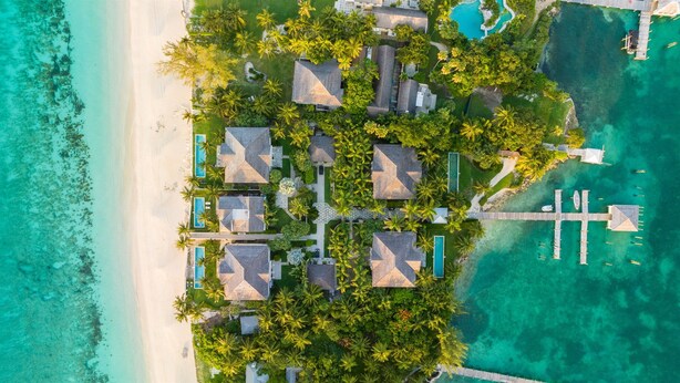 An aerial view of a resort with multiple bungalow-style accommodations, a central pool, and a pier extending into turquoise waters. - Paradise Beach Villa, OCEANFRONT~Paradise Island~ (Paradise Island)