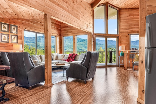 The open-plan living area on the upper level is anchored by a wall of windows and soaring vaulted ceilings. Comfortable seating, warm wood tones, and that view —always the view. Step through the door and onto the balcony with the Smokies spread before you.