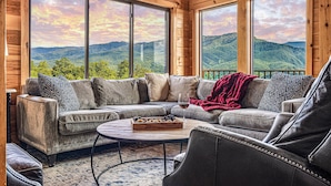 Ein gemütliches Blockhaus-Interieur mit einer großen Couch, einem Couchtisch und Bergblick durch große Fenster.
