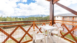 Un balcón con una mesa y sillas, que ofrece vistas a un paisaje montañoso y un edificio al fondo.