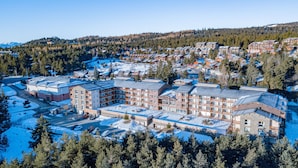 Un gran hotel con varios pisos y un patio central, rodeado de terreno cubierto de nieve y un bosque denso.