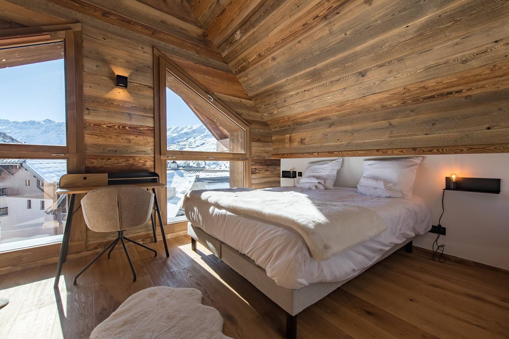 Een gezellig houten slaapkamer met een groot bed, een stoel en uitzicht op besneeuwde bergen.