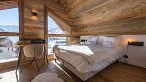 A cozy wooden cabin bedroom with a large bed, a chair, and a view of snowy mountains. - Olvera 501 - New apartment on the slopes (VALMEINIER)
