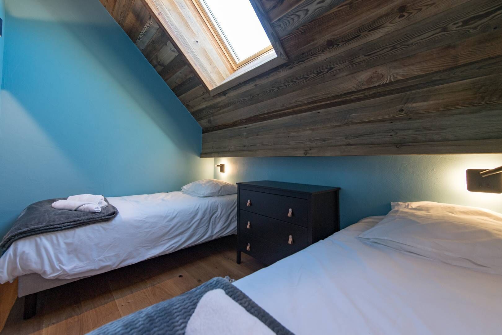 A bedroom with two beds, a wooden ceiling, and a skylight.