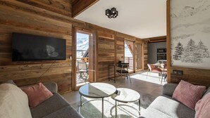 A modern living room with a large TV, a dining area with a table and chairs, and a balcony with a view of snow-capped mountains. - Olvera 501 - New apartment on the slopes (VALMEINIER)
