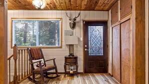 Un interior de madera con una mecedora, una cabeza de venado montada en la pared y una puerta con un panel de vidrio decorativo.