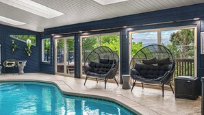 Ein überdachter Pool mit schwarzen Korbstühlen, Blick ins Freie und einer Holzbalkendecke.