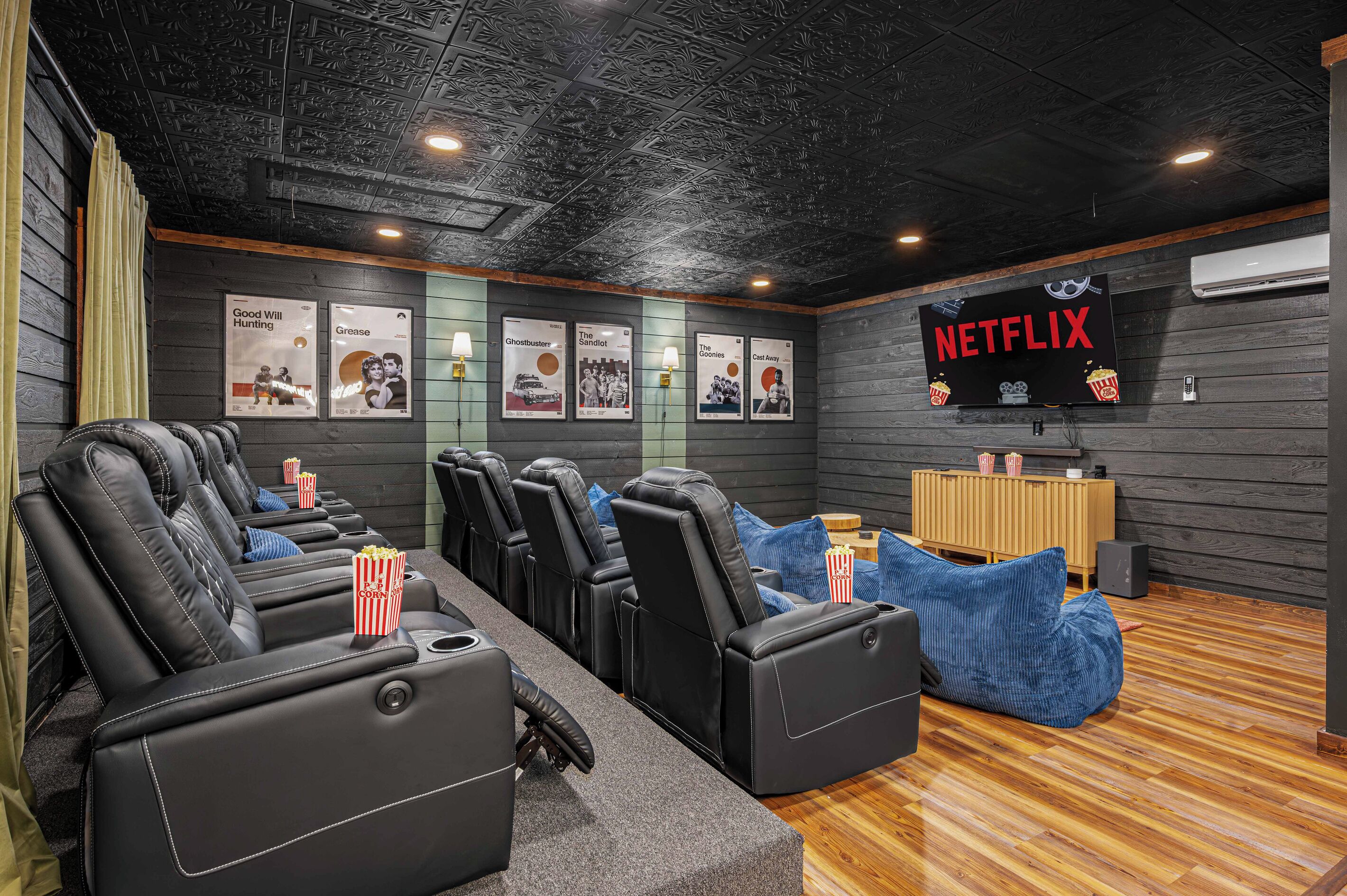 A cinema room with reclining seats, posters on the wall, a Netflix sign, and a wooden floor.