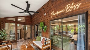 Ein modernes Interieur mit Holzwänden, einem Deckenventilator, einer Couch mit Kissen und einer großen Glasdoor, die nach draußen führt.