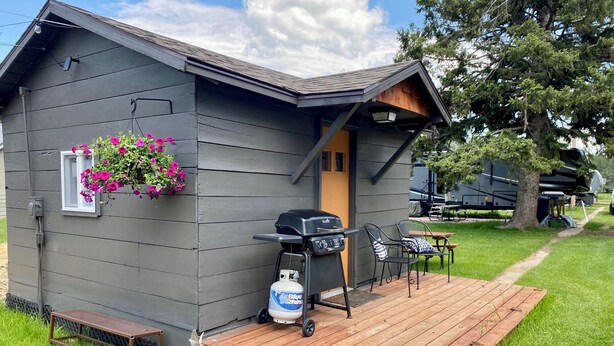 A small cabin with a porch, a grill, and a hanging flower basket.