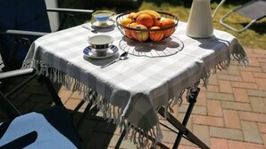 Una mesa al aire libre con mantel a cuadros, una cesta de frutas, una jarra y una tetera.