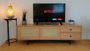 Un televisor sobre un mueble de madera con el logotipo de Netflix, una lámpara y dos macetas.
