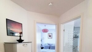 Un pasillo que da a un dormitorio con cama, cómoda y puerta al baño.