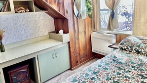 Une chambre à coucher comprenant un lit, un radiateur, une fenêtre avec des rideaux, une armoire en bois et une étagère avec des objets décoratifs.