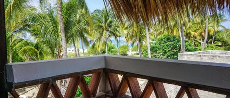 A wooden balcony railing with a view of palm trees and a beach.