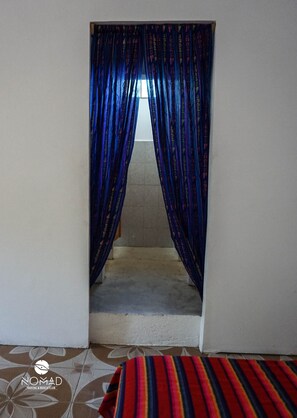 Una puerta con cortinas azules, un suelo estampado y una cama con manta a rayas.
