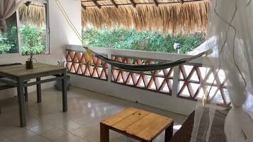 Una habitación con una hamaca, una mesa de madera y vistas a la vegetación a través de una ventana con celosía.
