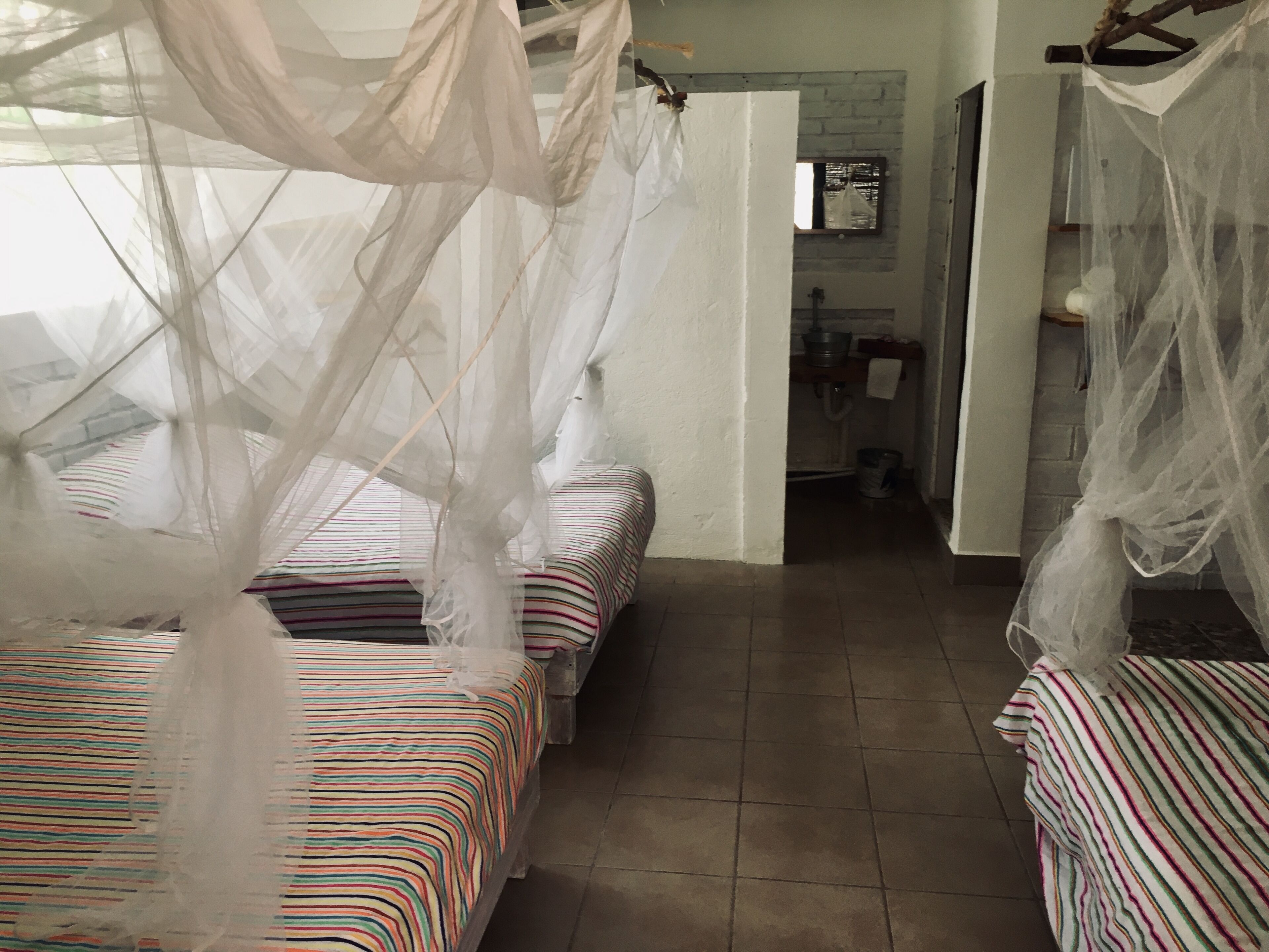 A room with two beds, each covered with striped bedding and a white canopy.