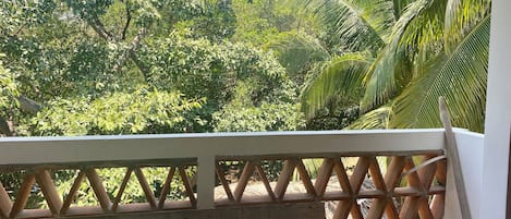 A balcony with a wooden lattice railing, a white pillow, and a bed with a patterned bedspread.