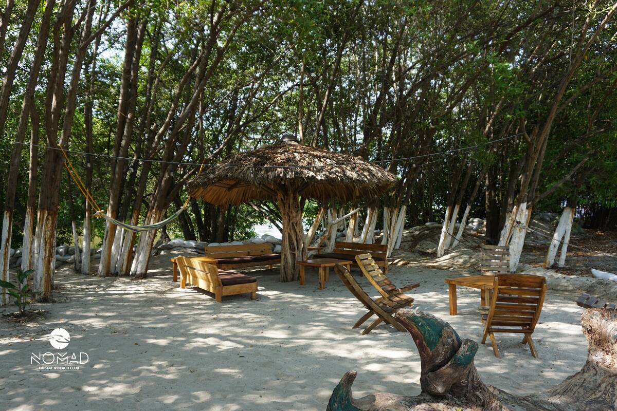 Un décor de plage avec des meubles en bois, un parasol en chaume et un hamac.