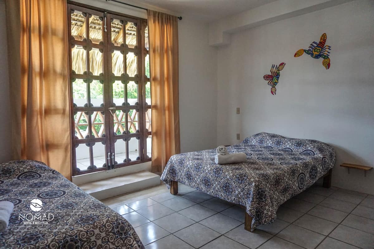 Une chambre avec deux lits, une fenêtre avec des rideaux et un mur orné d’une fresque représentant des poissons.