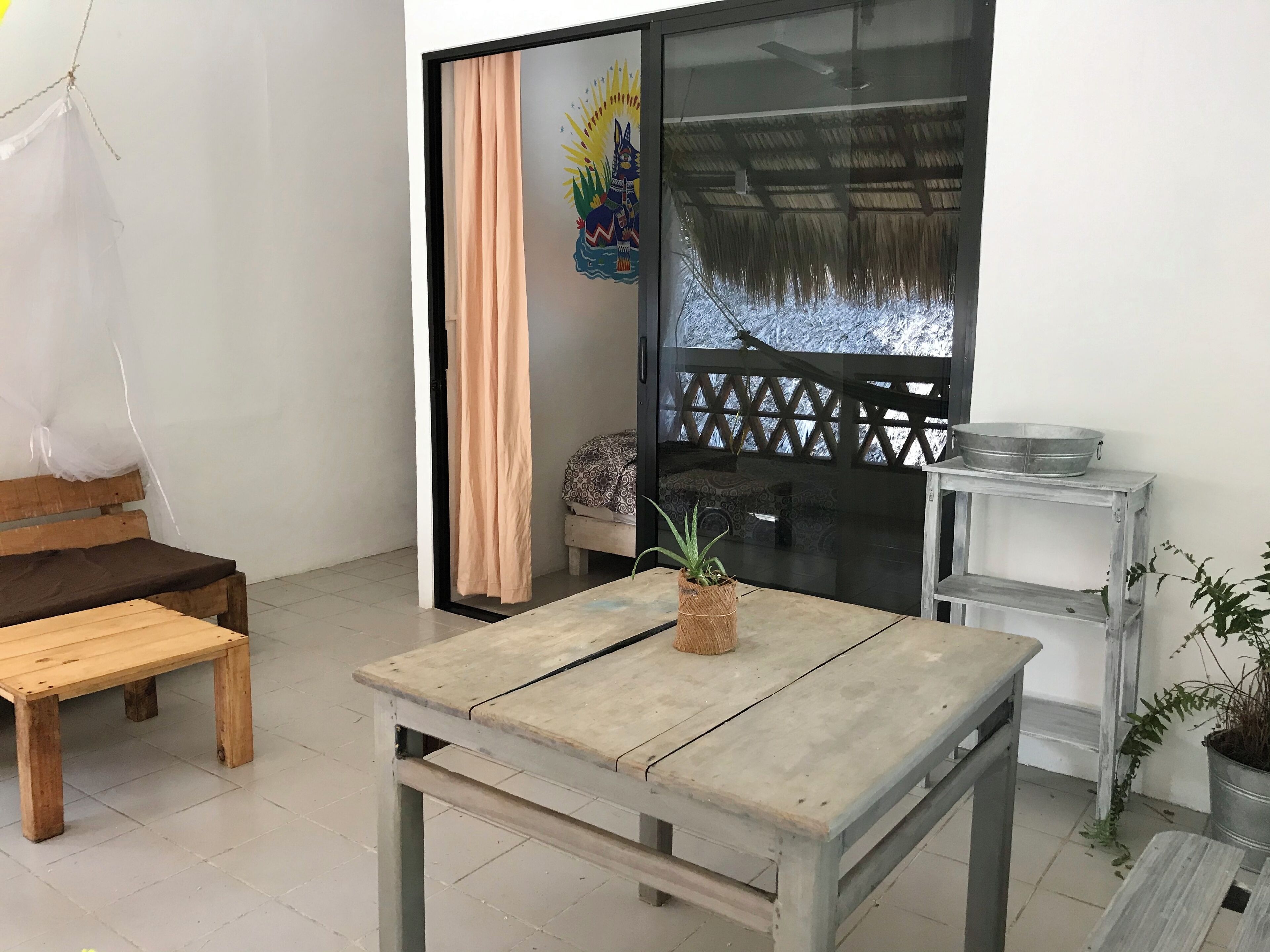 A room with a wooden bench, a small table, a potted plant, a metal shelf, and a decorative painting on the wall.