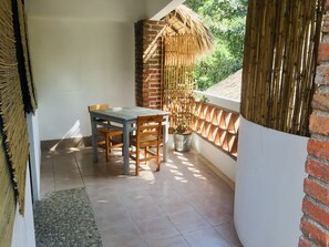 Un pequeño patio con una mesa, sillas, una planta en maceta y una cerca de bambú.
