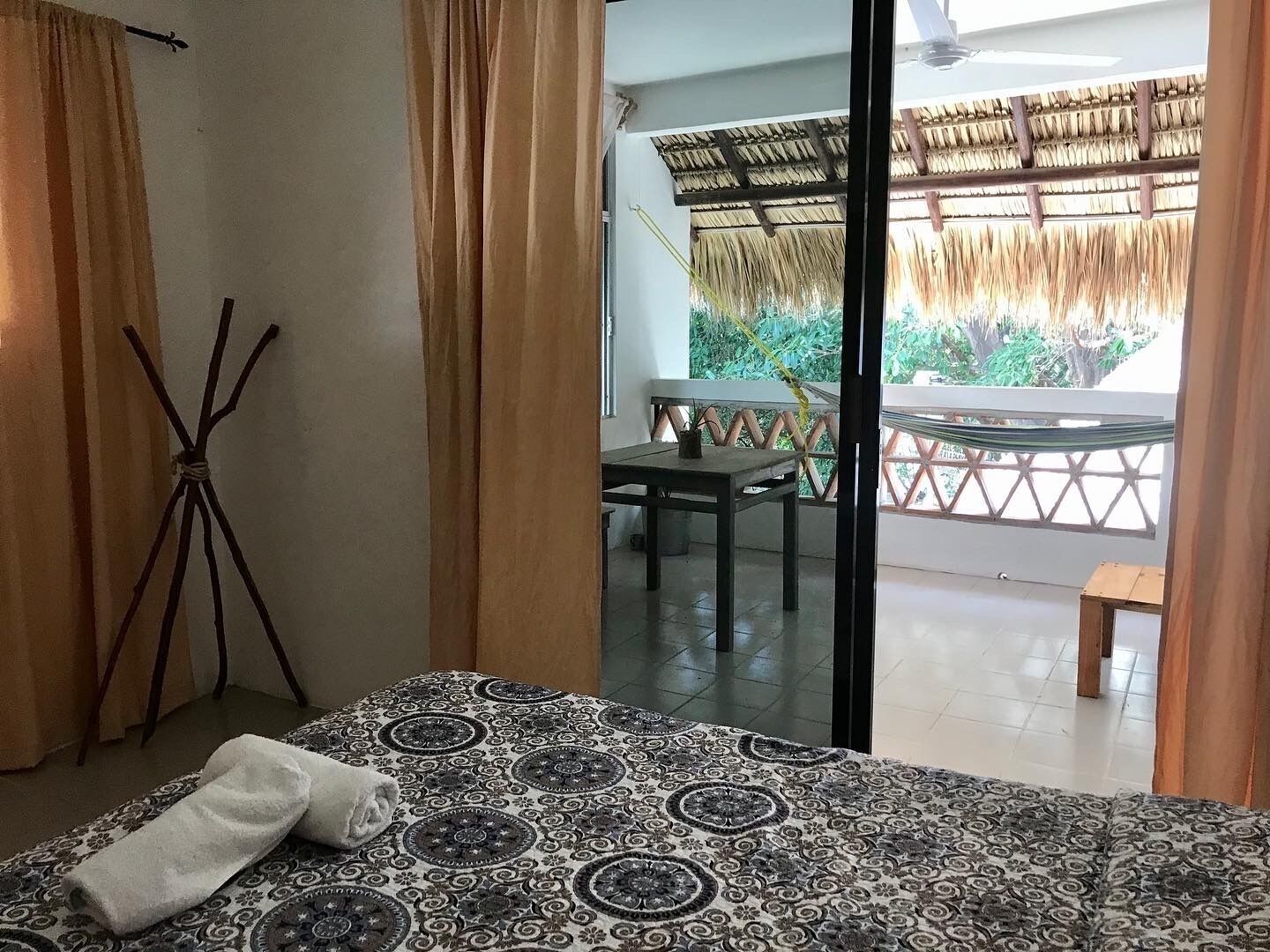 Une chambre avec un lit, une table et une vue sur un balcon doté d’un toit de chaume.