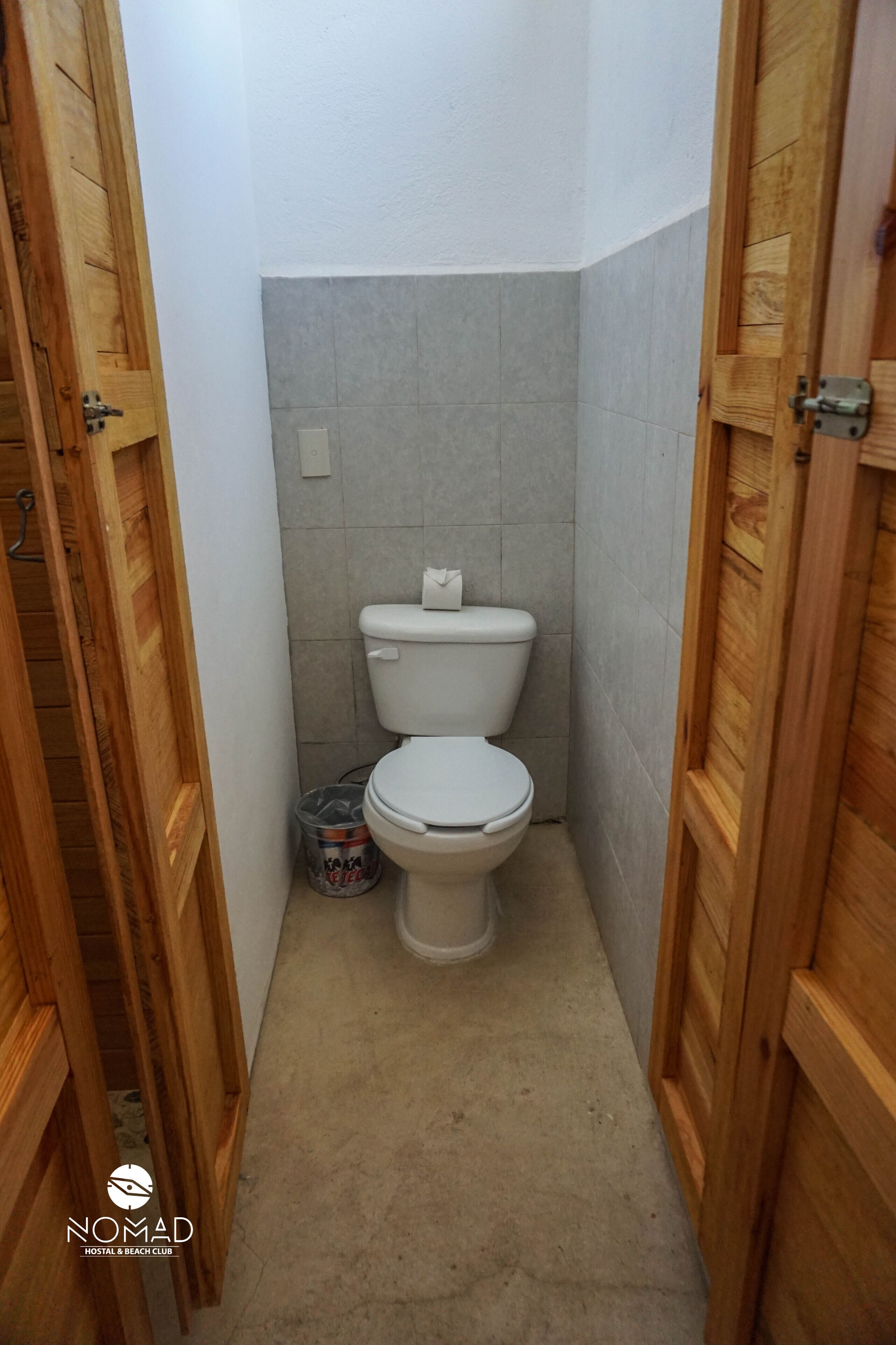 A small, narrow bathroom with a white toilet, grey tiles, and wooden doors.