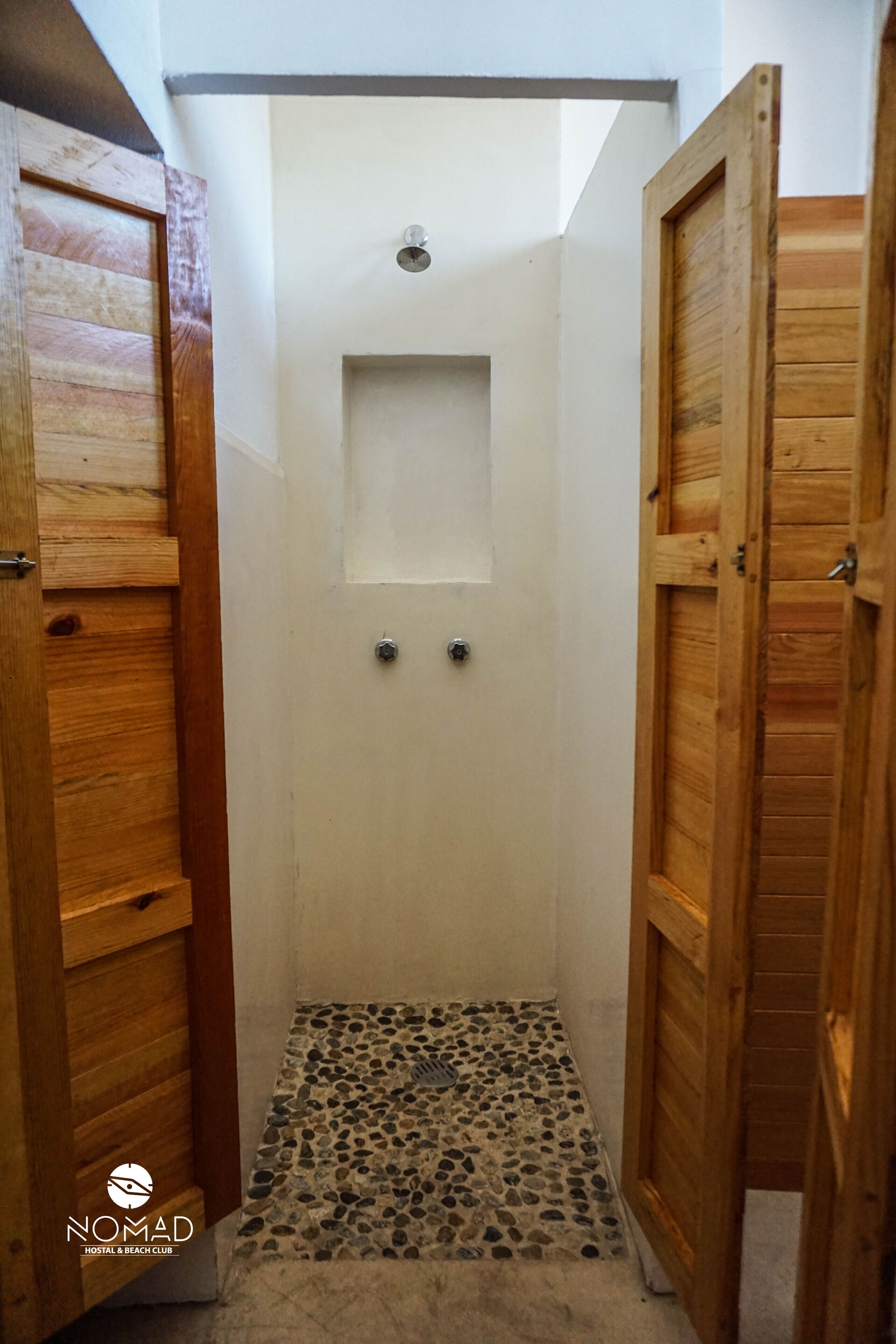 A narrow shower area with a tiled floor and a small shelf above the door.