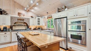 Une cuisine spacieuse avec des meubles blancs, un grand îlot central en bois, des appareils électroménagers en acier inoxydable et un plafond au style rustique.